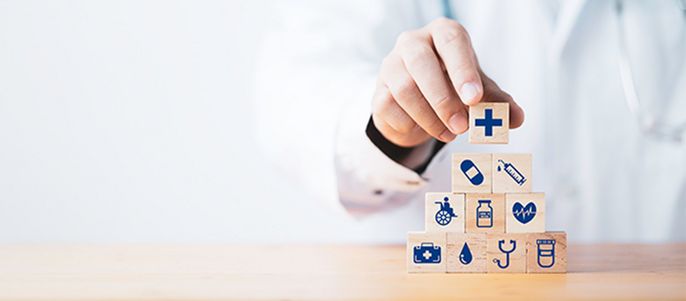 Eine Person, bei der es sich vermutlich um einen Arzt handelt, stapelt Holzklötze mit verschiedenen medizinischen Symbolen darauf.