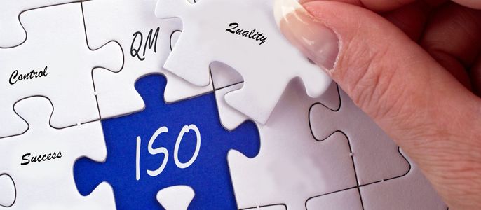 Ein Puzzle mit verschiedenen Teilen, die jeweils mit einem Begriff aus den Bereichen Geschäftsprozesse und Qualitätsmanagement beschriftet sind. Auf dem zentralen, blau gefärbten Teil steht "ISO", und die umliegenden Teile enthalten "Qualität", "Kontrolle", "Erfolg", "Optimierung", "Prozesse" und "Kosten".