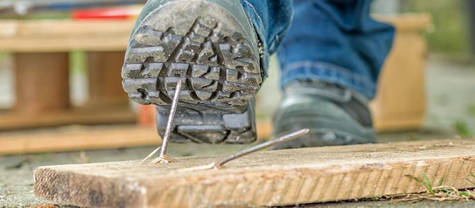Ein Schuh, der auf einen Nagel tritt, so dass dieser die Sohle des Schuhs durchbohrt.