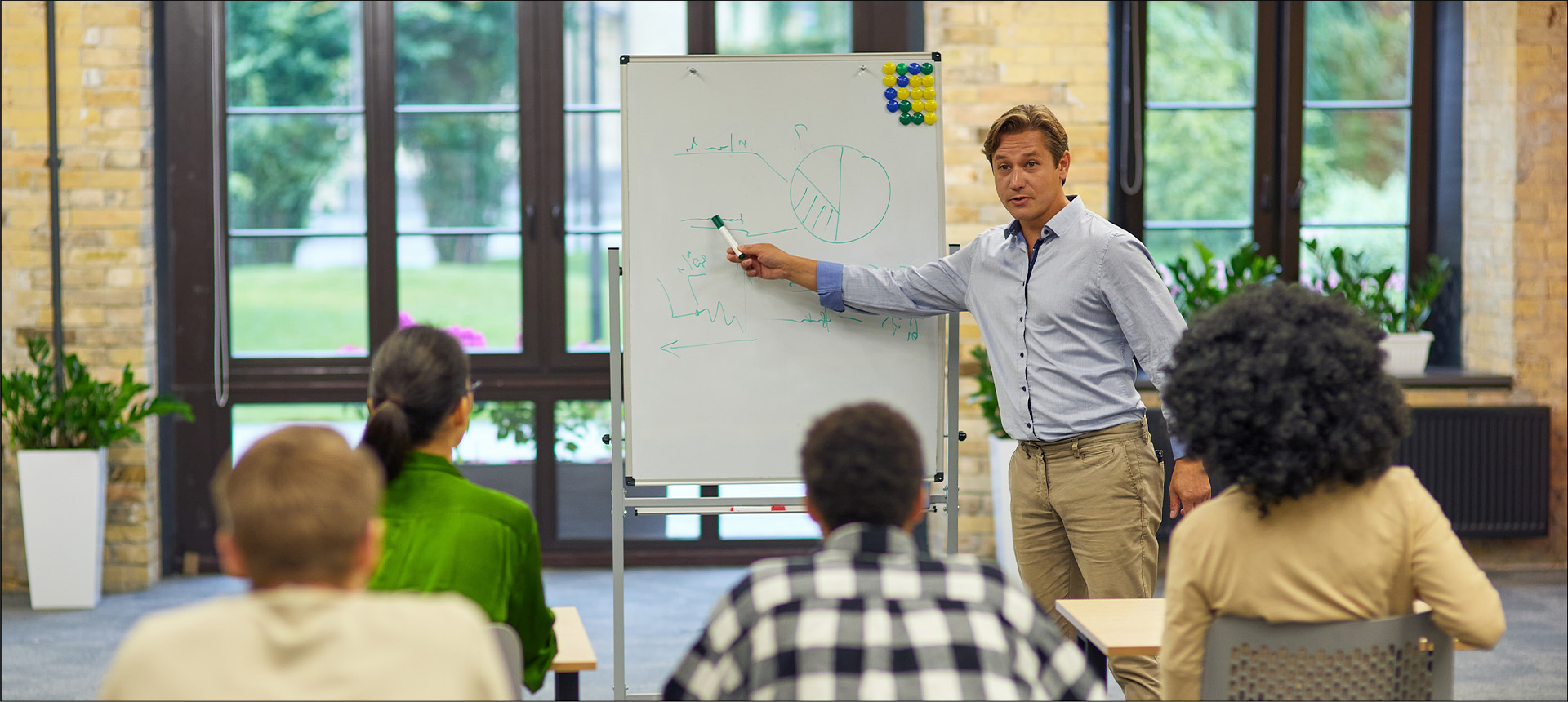 Eine Person, die etwas an ein Whiteboard zeichnet und es einigen Zuhörern erklärt.